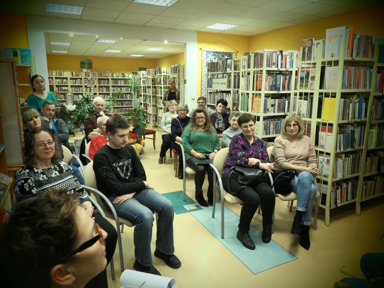 czytelnicy siedzą na krzesłach w bibliotece w zblewie podczas spotkania autorskiego