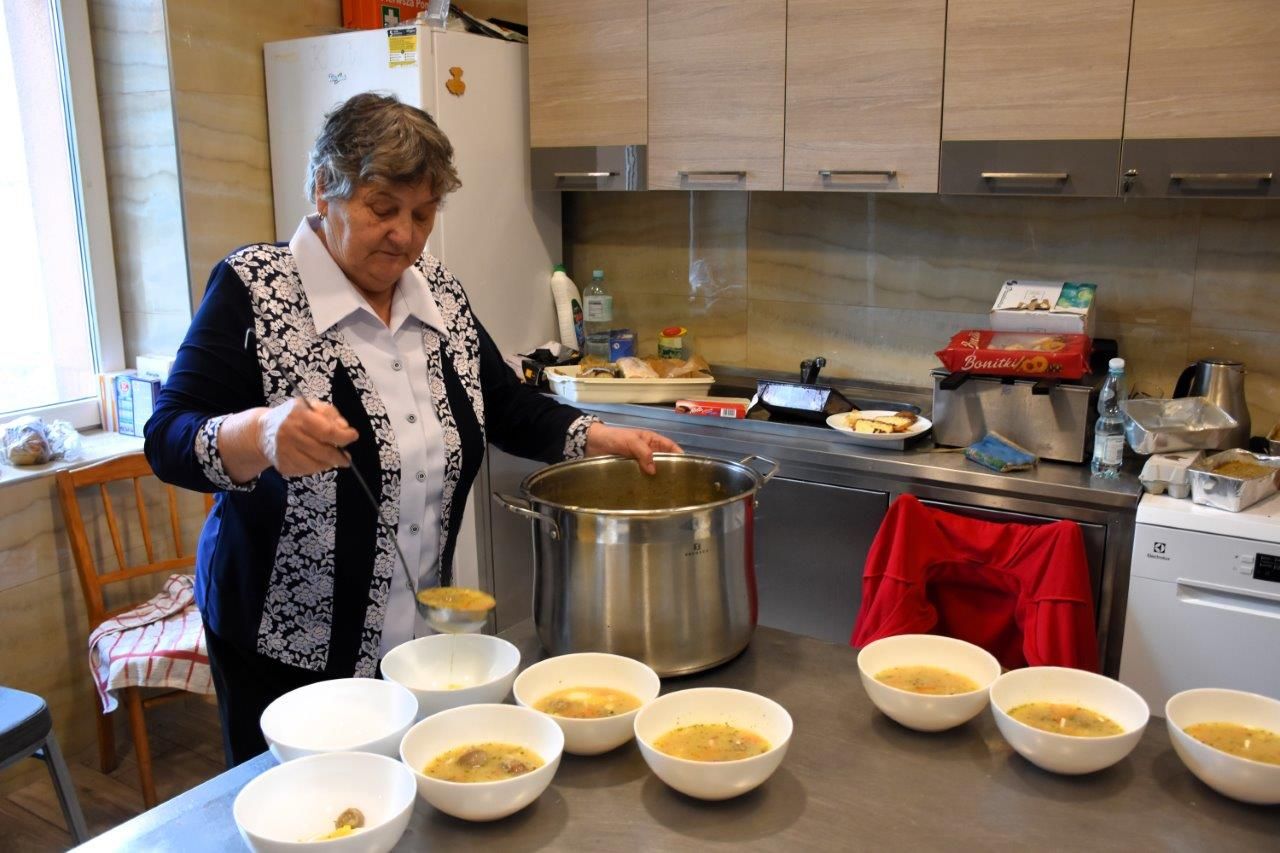 zdjęcie przedstawia kobietę w kuchni, która nalewa zupę