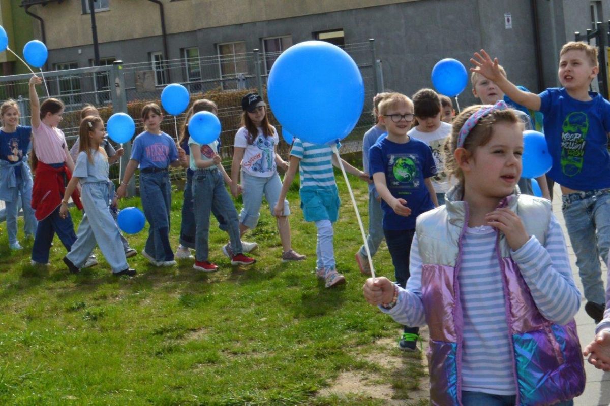 dzieci ubrane na niebiesko z niebieskimi balonikami naszerują na ulicach Zblewa