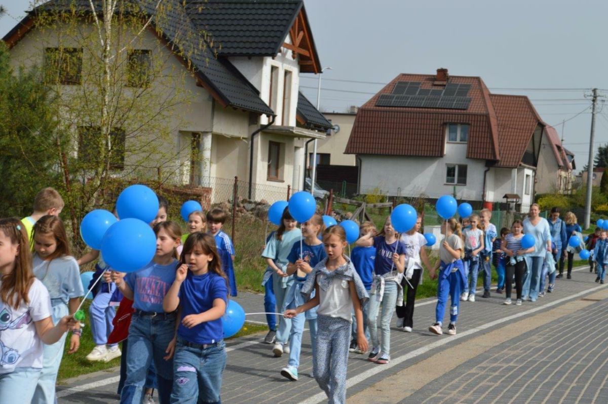 dzieci ubrane na niebiesko z niebieskimi balonikami naszerują na ulicach Zblewa