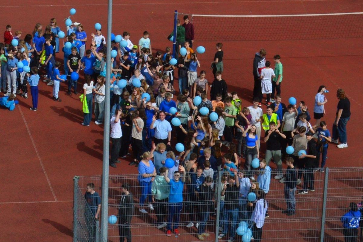 dzieci ubrane na niebiesko z niebieskimi balonikami naszerują na ulicach Zblewa