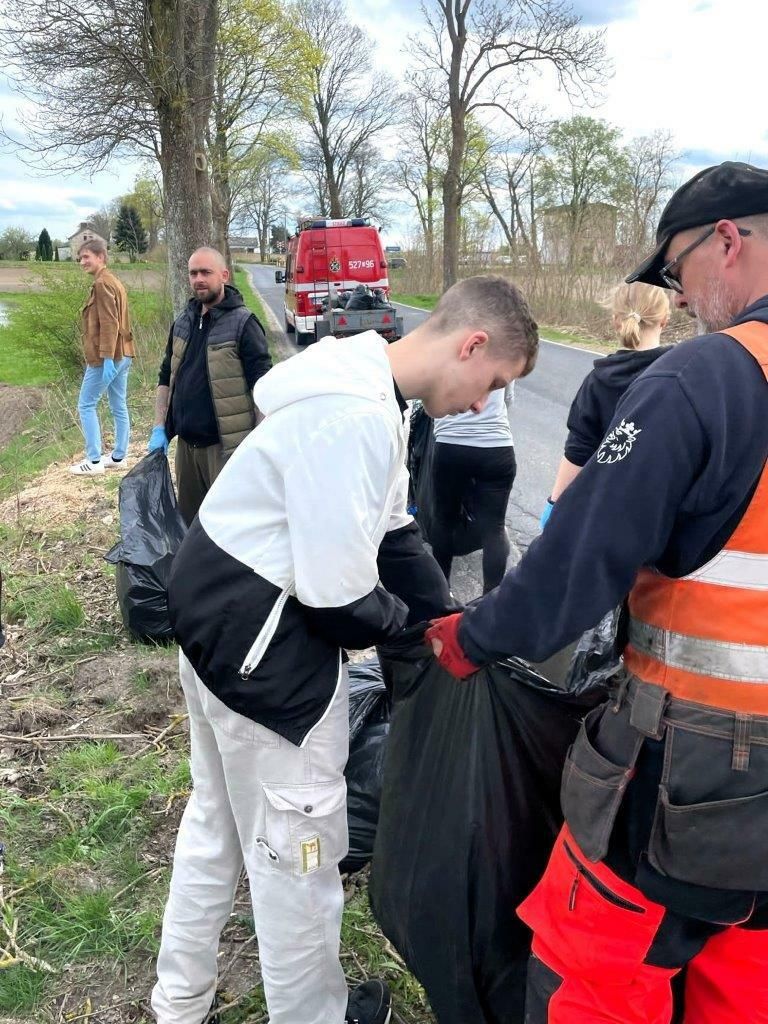 grupa ludzi z workami sprząta pobocza drogi