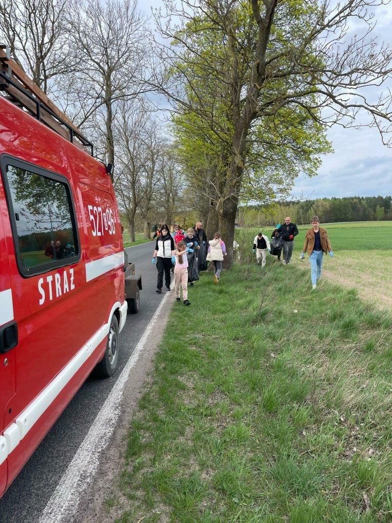 grupa ludzi z workami sprząta pobocza drogi