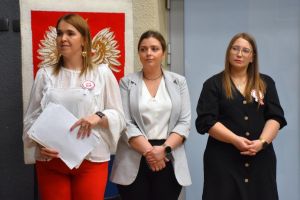 trzy kobiety stoją na tle wizerunku białego orła na sali ośrodka kultury