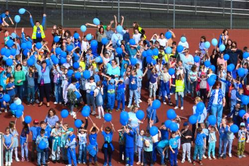grupa dzieci ubrana na niebiesko z niebieskimi balonikami stoi na szkolnym boisku